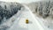 Concept of auto travel during winter holiday season. One yellow car is driving on snow along mountain road near forest. Aerial