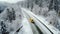 Concept of auto travel during winter holiday season. One yellow car is driving on snow along mountain road near forest. Aerial