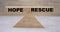 Concept of the balance of words HOPE win and RESCUE on wooden scales on a light background