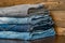 The concept of casual style in clothing. A stack of jeans in different shades of color on a wooden table.