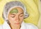 The concept of cosmetology. Close-up of a beautician applying a green mask with a brush on a woman`s face