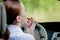 Concept of danger driving. Young woman driver red haired teenage girl painting her lips doing applying make up while driving the