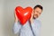 The concept of declaration of love or Valentine`s Day greeting. Photo of man peeking out from behind red inflatable balloon in