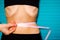 Concept of diet, proper nutrition and health. Thin woman measures belly with centimeter tape on a blue wooden background