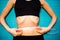 Concept of diet and proper nutrition. Thin woman measures the belly with a centimeter tape on a turquoise wooden