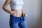 The concept of diet and weight loss. A woman in large jeans on a blue background shows her slender stomach. Liposuction