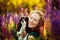 The concept of a dog and a woman. A young woman hugs and kisses her beautiful dog Cavalier King Charles Spaniel in purple lupine