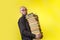 Concept of education. A bald man with a beard and glasses, holding a large stack of books. Yellow background. Copy space