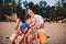 The concept of a family vacation. Young family sitting on a bench in the evening on a sandy beach. Mom and Dad kiss, the older bro