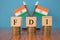 Concept of FDI or foreign Direct Investment on India in wooden block letters on stack of coins with Indian Flag as a background