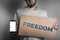 Concept of freedoms and human rights. A man with a cardboard and a phone in his hand. Text freedom and mock up. Dark color