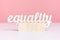 The concept of gender equality. The word equality on three wooden cubes on a pink background. Mockup for your phrase or characters