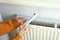 Concept of heating season with girl holds thermometer near radiator