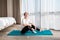 Concept of home training and yoga. A young woman sits on a sports mat and smiles. Windows and the interior of the bedroom in the