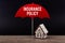 Concept of house insurance. Wooden house under red umbrella with text Insurance Policy