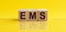 Concept image a wooden block and word - EMS - Express Mail Service on yellow background