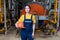 The concept of industrial manufactory. A young smiling woman in uniform holds a safety helmet in her hand and poses while standing