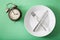 Concept of intermittent fasting, ketogenic diet, weight loss. fork and knife crossed on a plate and alarmclock
