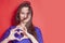 Concept: Love is blind. Portrait of pretty romantic young woman making a heart gesture with her fingers against red background.