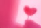 Concept modern abstract background of shadow heart in hand on a pink wall