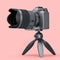 Concept of nonexistent silver DSLR camera with tripod isolated on pink.