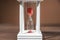 The concept of passing time. White hourglass with red sand inside on a wooden textural background.