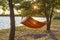 The concept of a picnic, solitude with nature and relaxation, a hammock against the backdrop of a lake in the rays of the setting