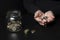 The concept of poverty. The hands of an elderly woman holding coins and jar of coins on dark background