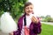 The concept of quick snacks by children. A contented eight-year-old girl in a lilac jacket eats cotton candy, close-up