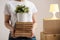 The concept of relocation and moving to a new home. Close-up, female hands hold a pile of books and a green plant in a