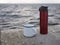 Concept of reusable accessories. friendship white mug and red thermos, who sit on the shore and admire the beauty of nature by the