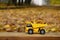 The concept of seasonal harvesting of autumn fallen leaves is depicted in the form of a toy yellow truck loaded with leaves again