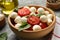 Concept of tasty eating with bowl of mozzarella, tomato and basil on gray table