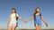 Concept tourism and travel. Girls, women travellers go holding hands on a background of blue sky. teamwork tourists