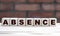 Concept word ABSENCE on cubes against the background of a brick wall