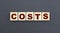 Concept word COSTS on wooden cubes on a gray background