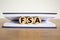 Concept word `FSA, flexible spending account` on wooden circles between pages of a book on a beautiful wooden table. White