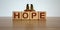 Concept word `hope` made on wooden cubes. Two metalic angeles