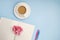 Concept workplace. White open notebook for notes, ballpoint pen, white cup of coffee with milk, pink flower on a blue background,