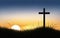 Conceptual black cross religious emblem silhouetted against a sky at dusk or dawn.