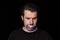 Conceptual portrait of young sad man with three colors duct tape over his mouth isolated on dark background. Censorship