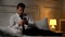 Concerned businessman texting with business partner, lying on bed in hotel room