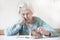 Concerned elderly woman sitting at the table counting money in her wallet.