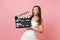 Concerned shocked bride woman in white wedding dress holding classic black film making clapperboard on pastel