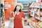 A concerned woman with a medical mask on her face walks in a supermarket. Concept of protection against coronavirus