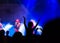 Concert crowd attending a concert, people silhouettes are visible, backlit by stage lights. Raised hands and smart phones are visi