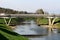 Concrete bridge over local river with low water level and visible rocks surrounded with grass filled river banks and trees