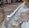 Concrete curbs are cemented along an evenly stretched line against the backdrop of a washed-out work area