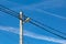 A concrete electric pole with a street lamp and lots of wires against a blue sky