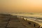 Concrete embankment with old wooden columns sticking out of the yellow sand against the background of the ocean waves under a